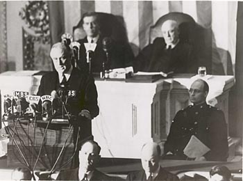 Pres. Franklin Delano Roosevelt delivers his "Day of Infamy" speech to Congress on December 8, 1941. Behind him are Vice President Henry Wallace (left) and Speaker of the House Sam Rayburn. To the right, in uniform in front of Rayburn, is Roosevelt's son James, who escorted his father to the Capitol (US National Archives)