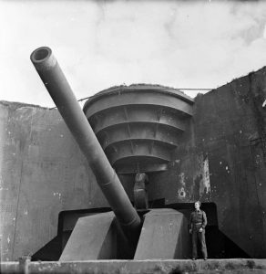 Soldier poses next to one of the German coastal guns captured by the Canadians at Cap Gris Nez, France, 1 October 1944 (Imperial War Museum B 10467)