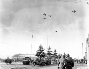 Troops of US 101st Airborne Division watching C-47 Skytrain aircraft delivering supplies to their unit, Bastogne, Belgium, 26 Dec 1944. (US Army Signal Corps)