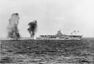 Bombs falling astern of HMS Ark Royal during attack by Italian aircraft during the Battle of Cape Spartivento, 27 Nov 1940; photograph taken from cruiser HMS Sheffield (Imperial War Museum: 4700-01 A 2298)