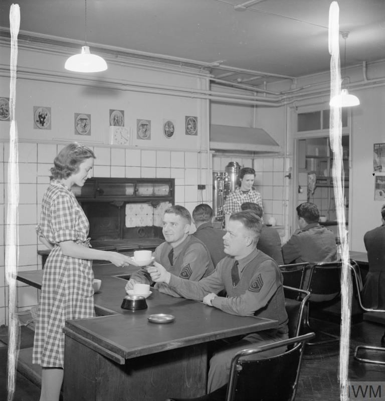 A female volunteer at the American Red Cross Eagle Club gives a cup of tea to one of several American soldiers making use of the canteen facilities at the club, WWII (Imperial War Museum: D 8333)