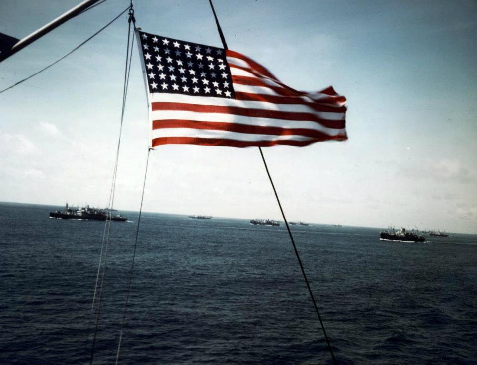 Convoy at Sea, World War II. The US flag frames a convoy of transports and cargo ships (US Army photograph, USA C-468)