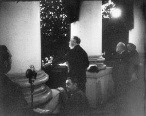 President Roosevelt addresses the crowd at the Christmas tree lighting ceremony from the White House South Portico on December 24, 1941. Churchill can be seen on the right. (FDR Presidential Library)