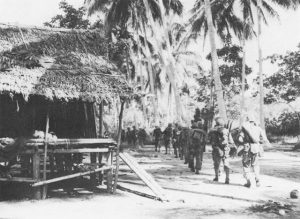 Troops of the US 128th Infantry Regiment passing through Simemi Village on way to Buna-Gona area, November 1942 (US Army Center of Military History)