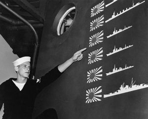 US sailor W.R. Martin points to scoreboard of light cruiser USS Boise from the Battle of Cape Esperance, 11-12 October 1942; the six Japanese ships claimed overstates actual enemy losses, not uncommon in night battles, Philadelphia Naval Shipyard, PA, November 1942 (US Naval History and Heritage Command: 80-G-36299)
