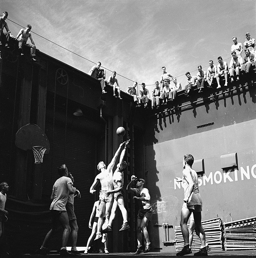 Navy personnel aboard USS Monterey play basketball in the forward elevator well June 1944; jumper on the left is Gerald Ford (US National Archives: 520764)