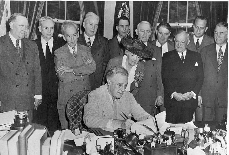 Pres. Franklin Roosevelt signs the G.I. Bill in the Oval Office, with (l to r) Bennett “Champ” Clark, J. Hardin Peterson, John Rankin, Paul Cunningham, Edith Rogers, J.M. Sullivan, Walter George, John Stelle, Robert Wagner, (unknown), and Alben Barkley; June 22, 1944 (FDR Library: NPx 64-269)