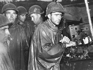 On Okinawa, men of the US 77th Infantry Division listen to the radio report of Germany’s surrender on May 8, 1945. One minute after this photo was taken, they returned to their combat posts. US forces on Okinawa celebrated V-E Day by training every ship and shore battery on a Japanese target and firing one shell simultaneously and precisely at midnight. (US National Archives: FA 41224- FA)